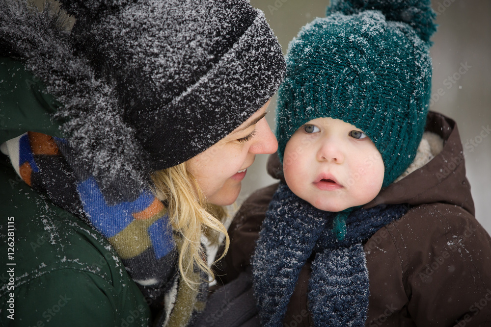 Portrait of young mother and little toddler boy in the winter forest. Family enjoying winter. Child and woman watching falling snow outdoors. Winter, Christmas and lifestyle concept. Portrait of young mother and little toddler boy in the winter forest. Family enjoying winter. Child and woman watching falling snow outdoors. Winter, Christmas and lifestyle concept.