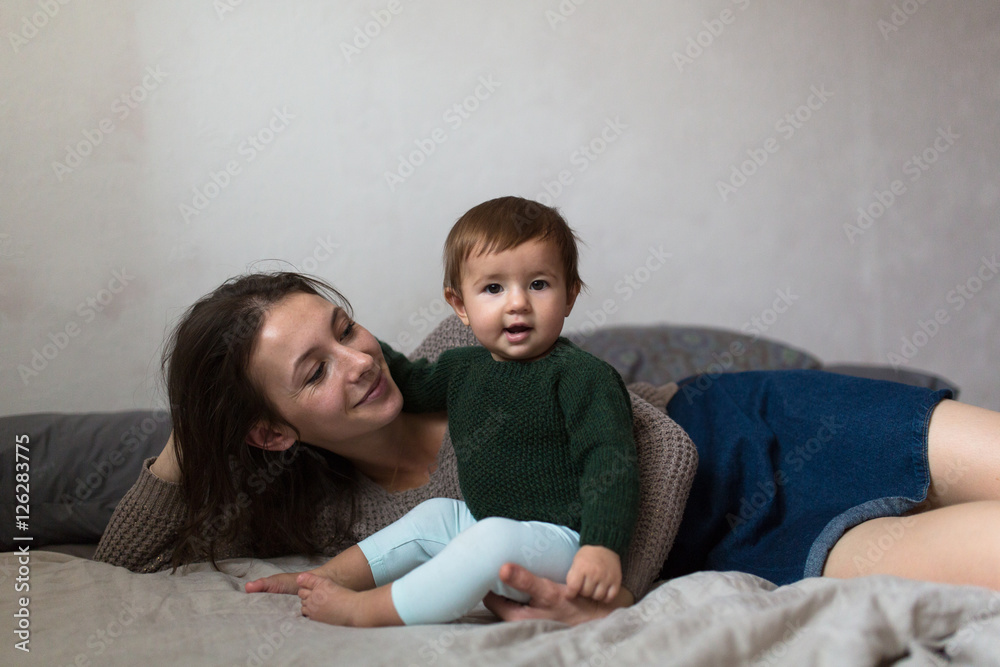 Shaggy young mother playing with baby on bed, concept of comf Shaggy young mother playing with baby on bed, concept of comf