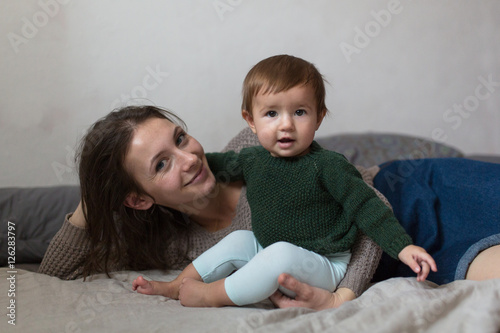 Shaggy young mother playing with baby on bed, concept of comf