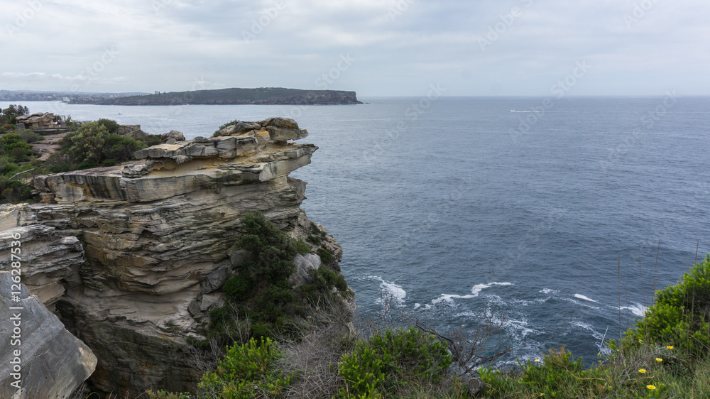 Steep rocky coast of Australia and the blue sea waves breaking on the rocks, the entrance to Sydney Harbour, Sydney