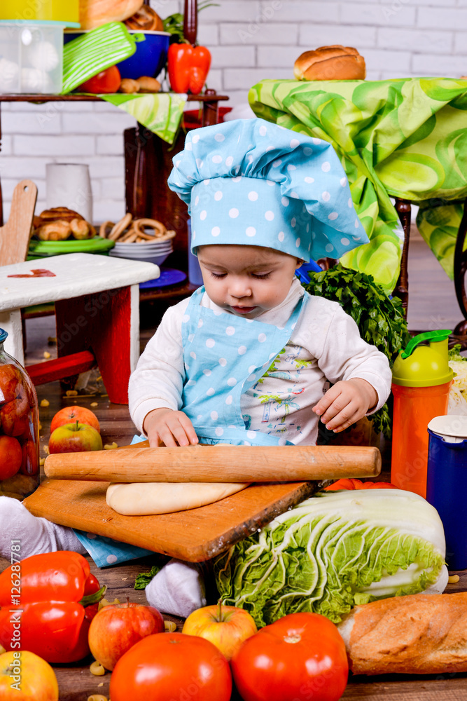 Little girl in a cook clothes rolls circle of dough on table Little girl in a cook clothes rolls circle of dough on table