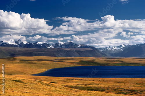 Clean deep blue lake on the background of snow ice covered mountains and glaciers rocks white clouds and bright sky, Plateau Ukok, Altai, Siberia, Russia