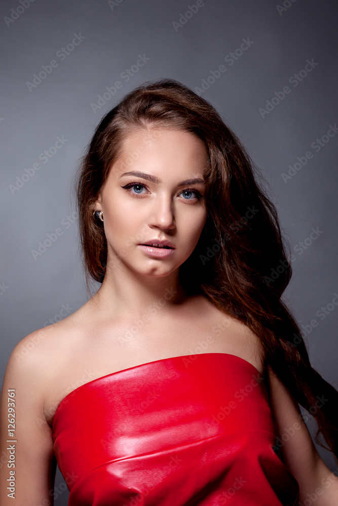 Portrait of the teenager in a red dress on a gray background