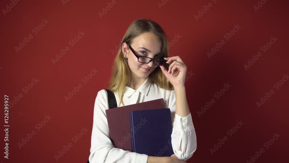 attractive happy smiling student blonde girl in glasses and white shirt with books on red background, student concept