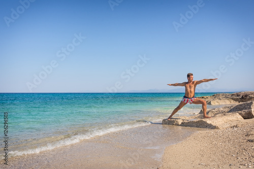 Adult man practicing yoga on the beach in Greece, in position wa