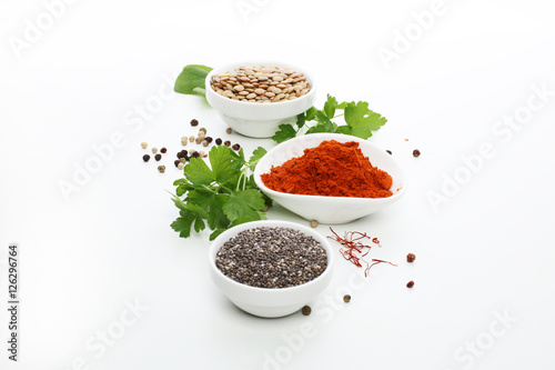 Bowls of assorted dried lentils and spices with vegetables over white