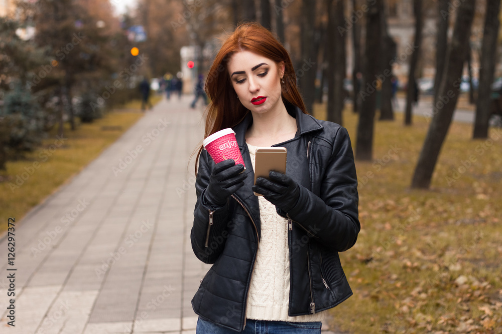 Portrait of girl with a cup of hot coffee and with mobile phone. New message. Girl walking through a street and type a message Portrait of girl with a cup of hot coffee and with mobile phone. New message. Girl walking through a street and type a message