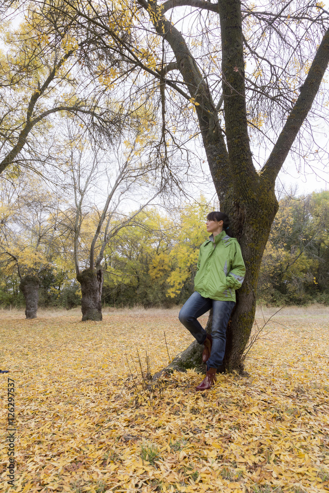 Woman sitting on a park bench with yellow leaves falling from trees