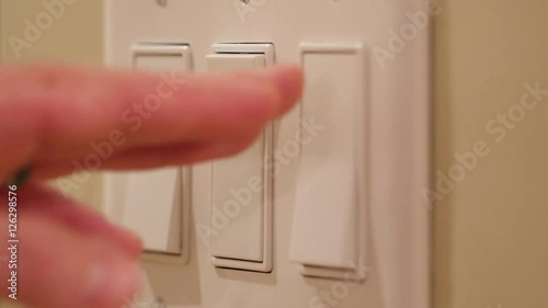 A hand turns on light switches in dark room