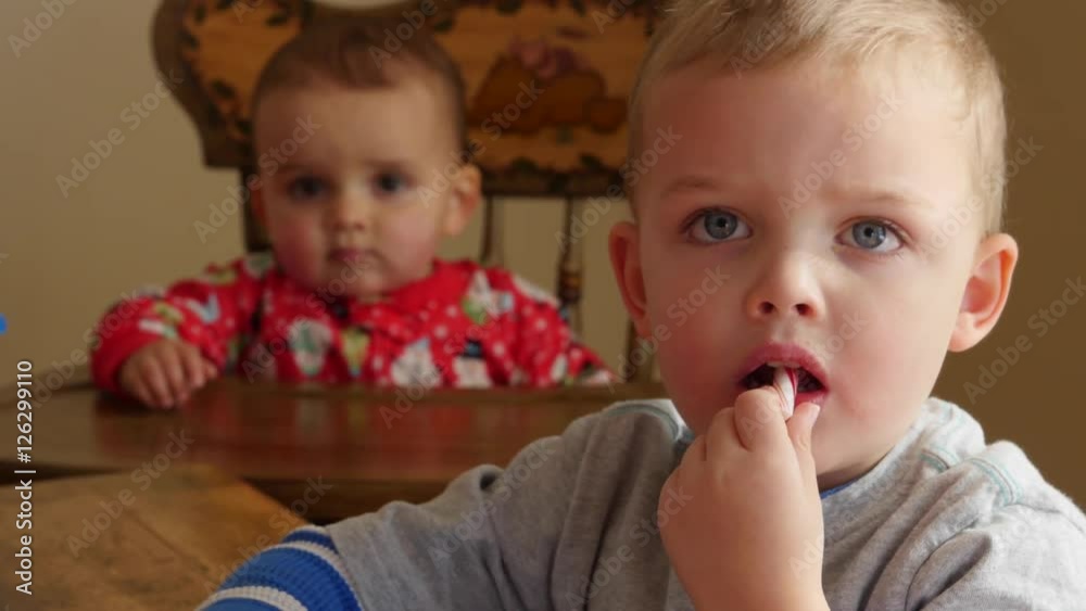 Little boy eats a candy cane while baby watches Little boy eats a candy cane while baby watches
