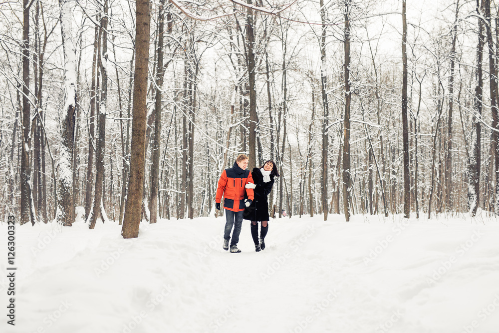 happy couple walking through a snowy forest in winter