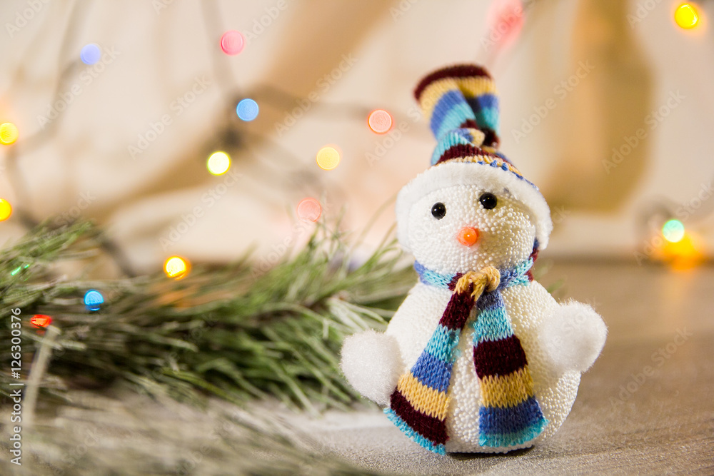 Obraz premium cute Christmas white snowman in a hat and a little Christmas toy tree in the background lights with place for text as substrate
