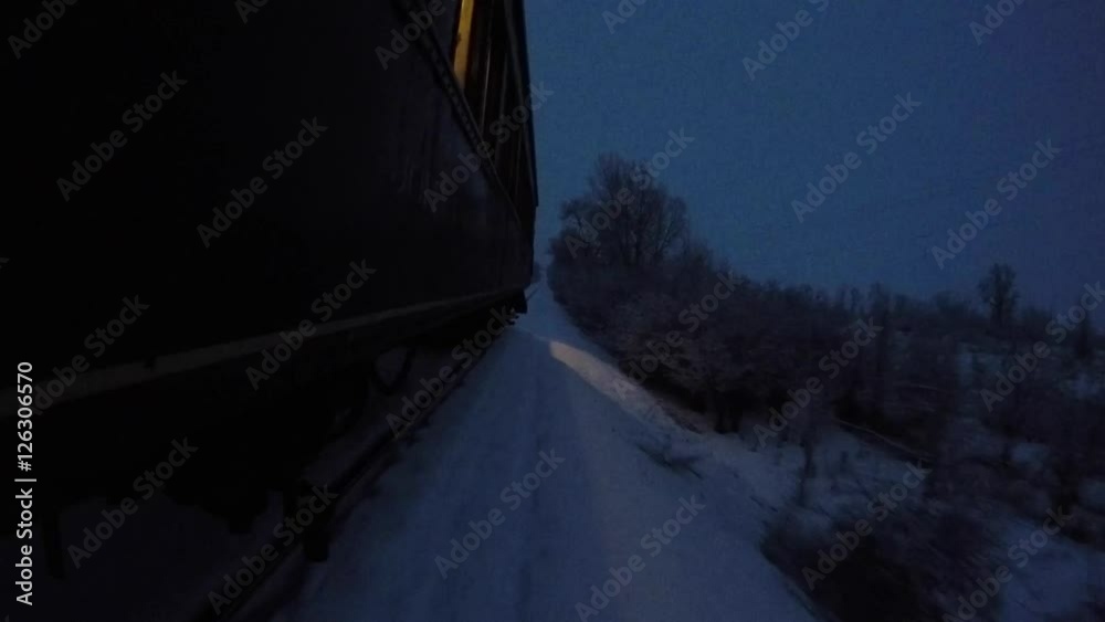 A cool exterior shot of a train passing through snowy winter fields during a snow storm at night