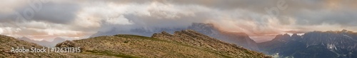 Panoramic mountain peak view from the Settsass in the Dolomites with warm colored cloudscapes hanging on the surrounding rocks.