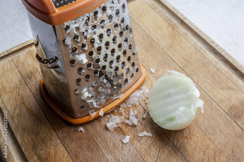 Half grated onion near metal standing grater on wooden cutting board