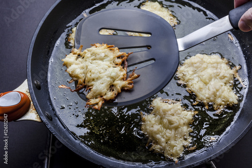 Turning over frying latkes with spatula in deep oil on pan from above