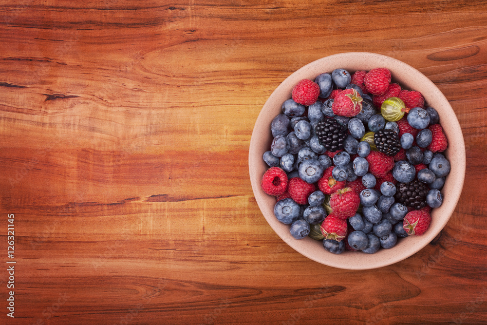 Brown ceramic plate with berries on the right of the wooden table with clipping path. Top view. Brown ceramic plate with berries on the right of the wooden table with clipping path. Top view.