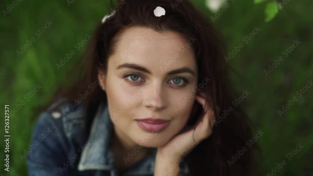 Young pretty smiling caucasian woman in jeans jacket sitting on green fresh grass near blooming spring tree. Youth, freshness, beauty, happiness concept. Young pretty smiling caucasian woman in jeans jacket sitting on green fresh grass near blooming spring tree. Youth, freshness, beauty, happiness concept.