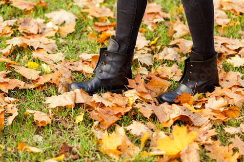 Female legs standing on green grass and autumn maple leaves