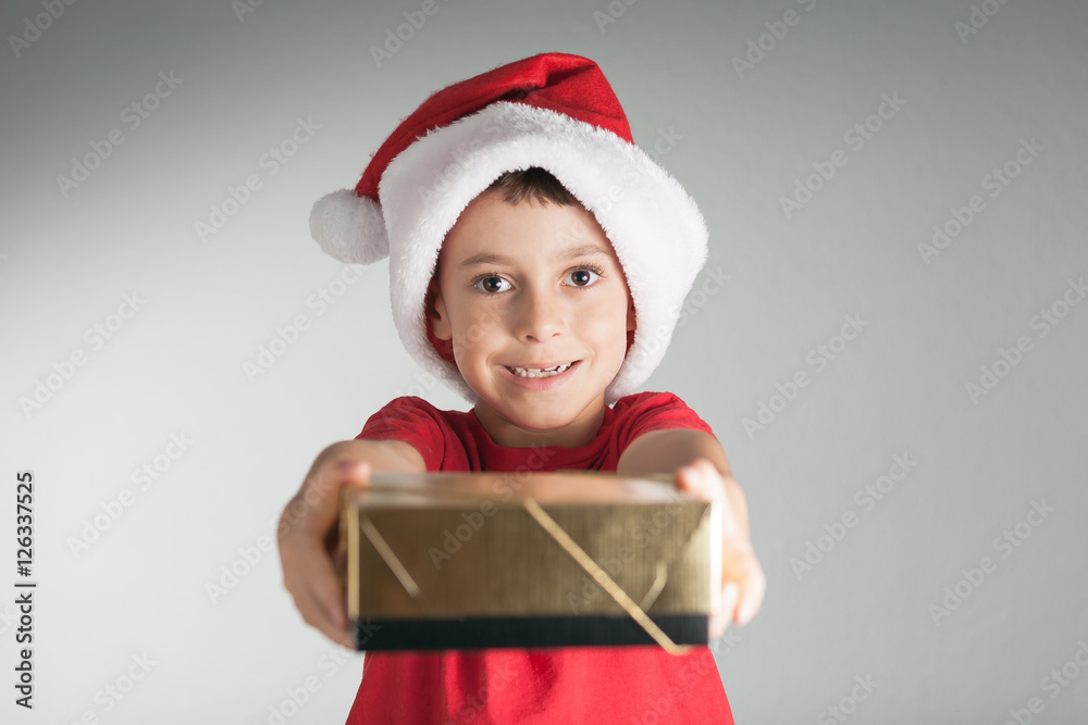 Smiling funny child in Santa red hat holding Christmas gift in hand. Christmas concept Smiling funny child in Santa red hat holding Christmas gift in hand. Christmas concept