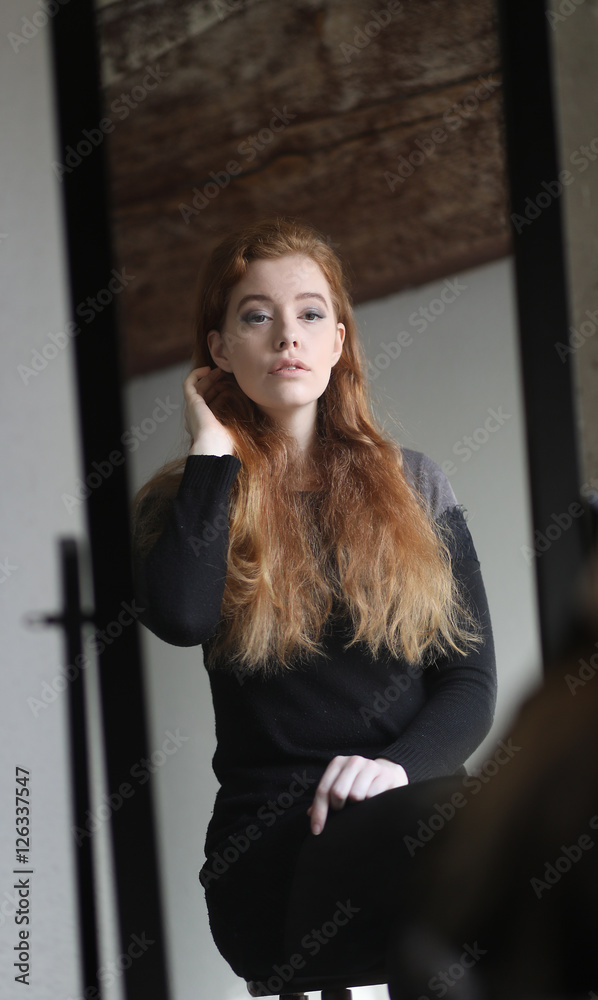 Fototapeta premium Red Haired Woman in Black Dress Looking at Herself in a Mirror