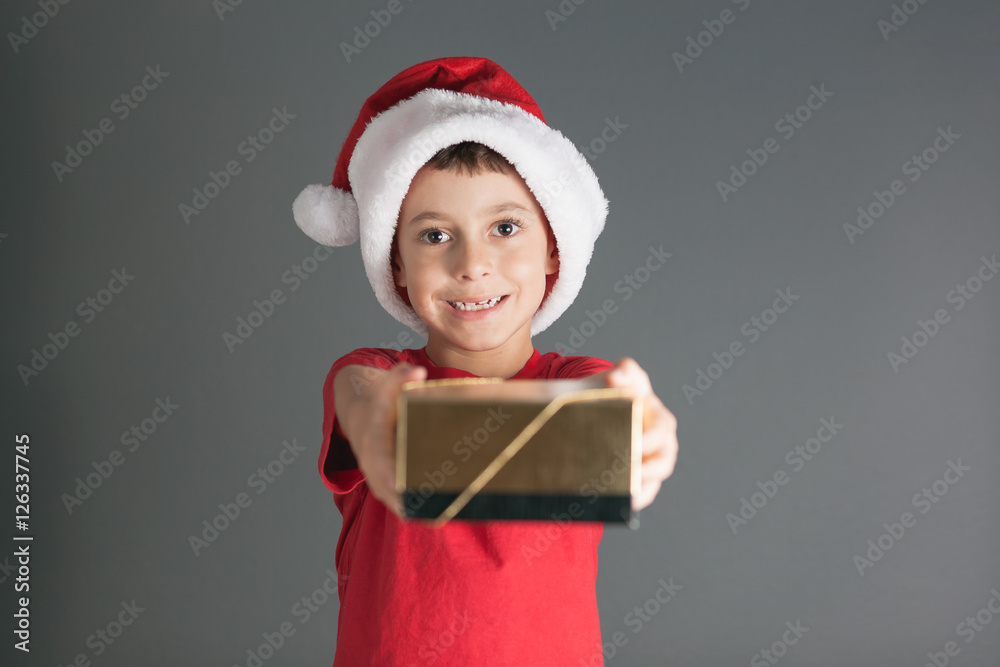 Smiling funny child in Santa red hat holding Christmas gift in hand. Christmas concept Smiling funny child in Santa red hat holding Christmas gift in hand. Christmas concept