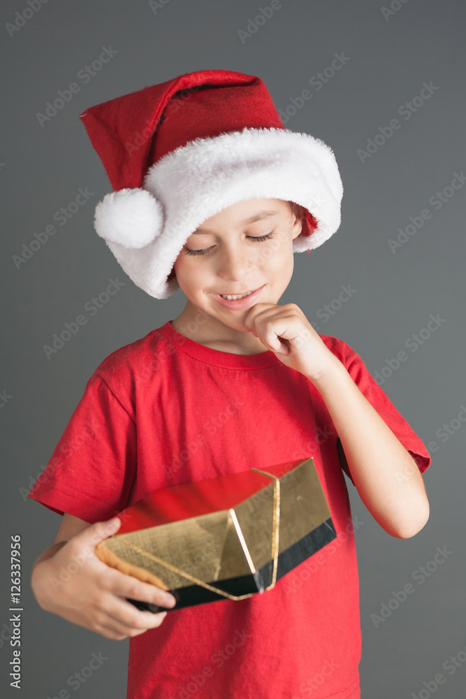 Smiling funny child in Santa red hat holding Christmas gift in hand. Christmas concept Smiling funny child in Santa red hat holding Christmas gift in hand. Christmas concept