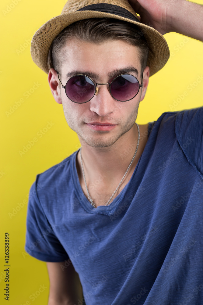 Cheerful young man in hat and sunglasses over yellow background