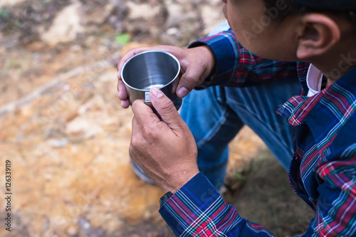 Man traveler hands holding cup of tea near the fire outdoors. Adventure, travel, tourism and camping concept. Hiker drinking tea from mug at camp. Coffee cooked over a campfire on the nature.