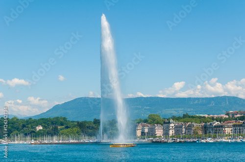 Geneva skyline with famous Jet d'Eau fountain and traditional boat at harbor district in Canton of Geneva, Switzerland