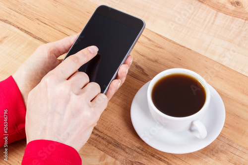 Hand of woman touching blank screen of mobile phone, cup of coffee