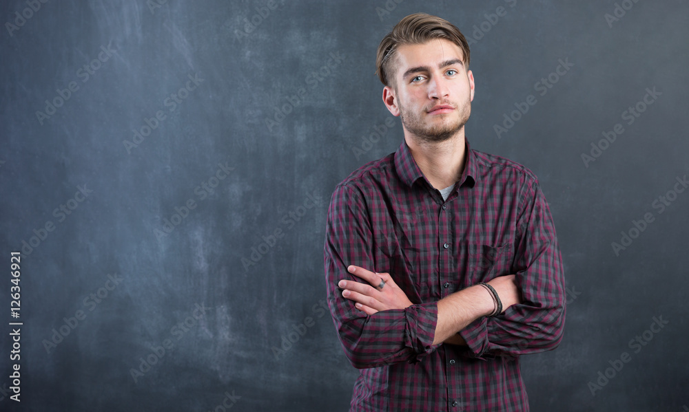 Happy young man standing with arms crossed over blackboard backg
