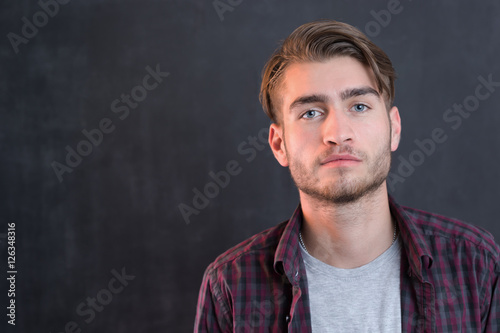 Handsome young student in shirt standing against blackboard