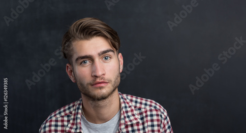 Handsome young student in shirt standing against blackboard