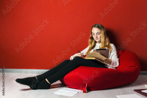 Young student girl studying sitting on the bag-chair near books and tablet pc photo