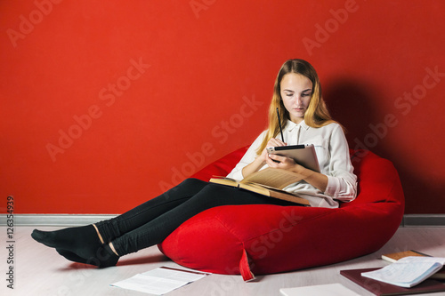 Young student girl studying sitting on the bag-chair near books and tablet pc photo
