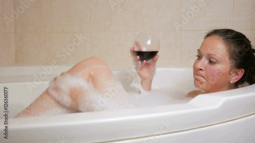 Beautiful girl taking a bubble bath with a glass of wine. A large white bath and joy on his face. relaxation concept photo