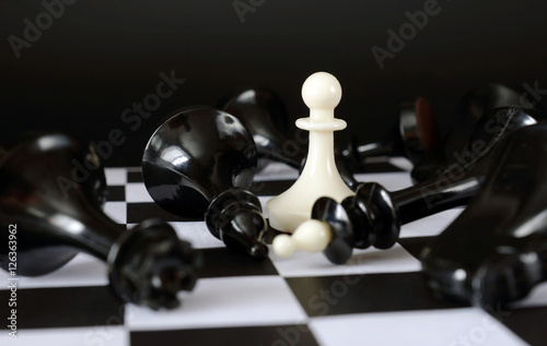 Pawn among fallen enemies. Winner and total victory. Concept with chess pieces against black background