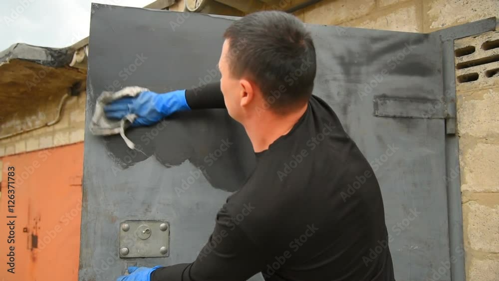 Preparation of a surface for painting. Performance of paintings. The man paints garage gate. Restoration of old gate. Washing of a surface Preparation of a surface for painting. Performance of paintings. The man paints garage gate. Restoration of old gate. Washing of a surface