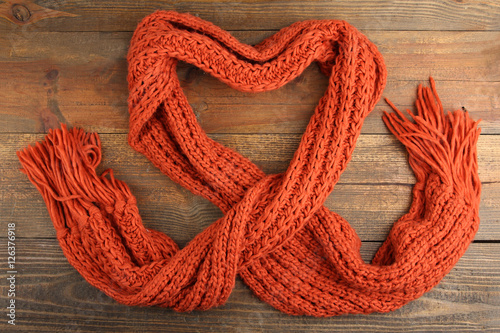 Knitted orange scarf in the shape of a heart on a wooden background