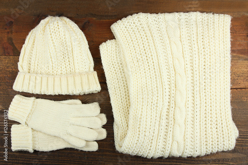 A white knitted hat, scarf and gloves on a wooden background
