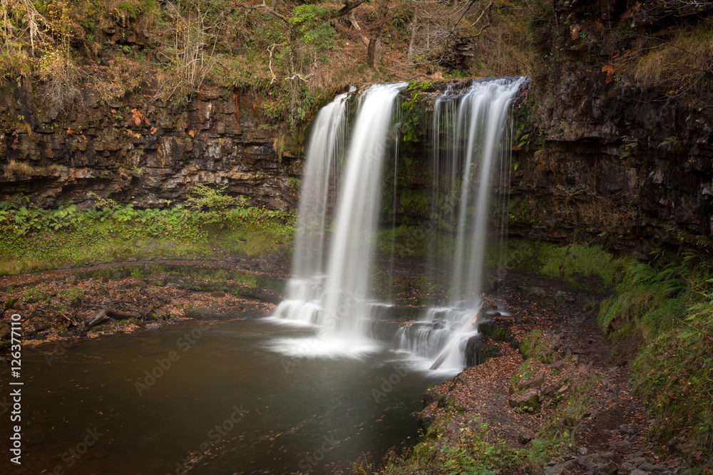 Obraz premium The Afon Hepste river plunges over a band of resistant gritstone to form the waterfall Sgwd yr Eira which translates into 'Fall of snow' and often refered to as the waterfall you can walk under. 