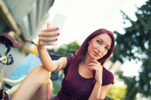 Red-haired girl sitting on the bench make selfie