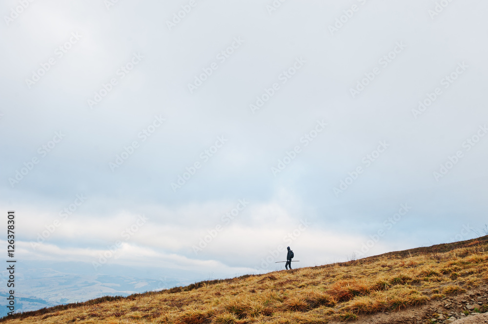 Man with a back pack walking down the mountain with stick at han