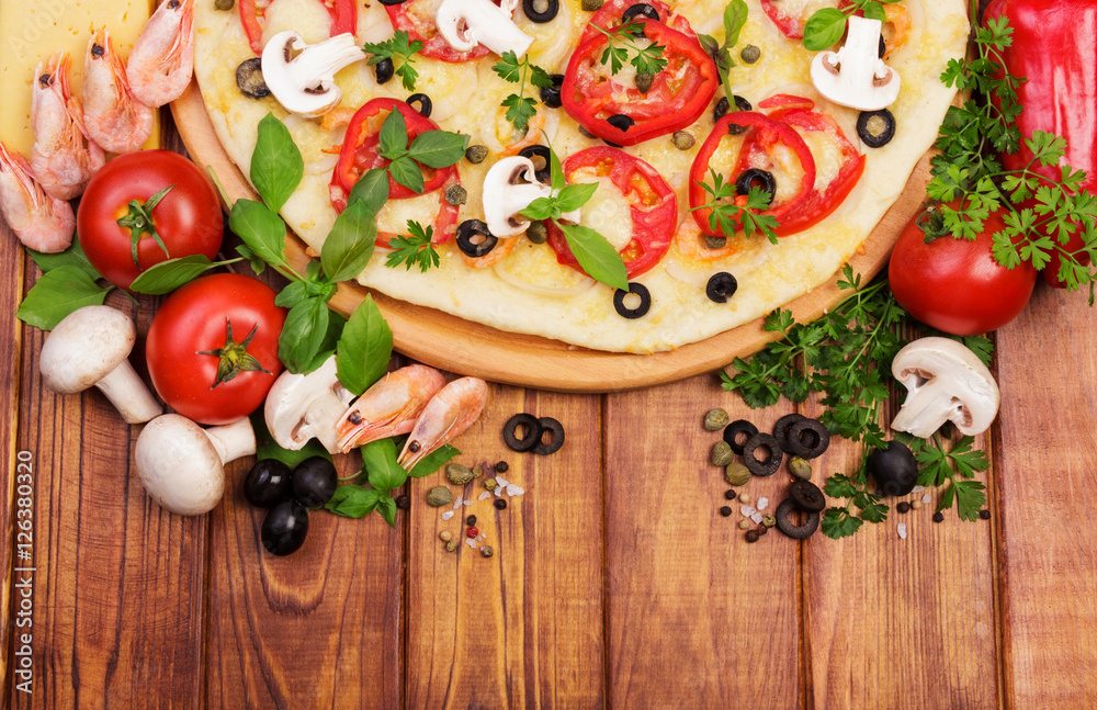 Pizza with shrimp, mushrooms, vegetables and greens on dark wood.