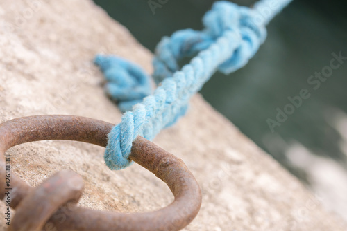 Blue rope tied to a rusty iron ring on the background of water