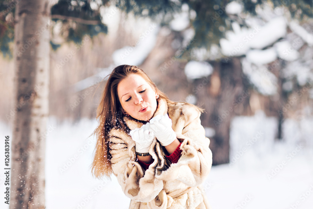 Young beautiful woman blowing snow in winter