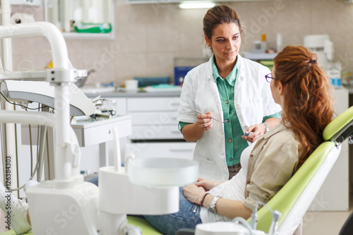 A professional female dentist  equipped with a bright smile  converses with her red hair female patient  carefully explaining the upcoming treatment  and ensuring her comfort throughout the process.