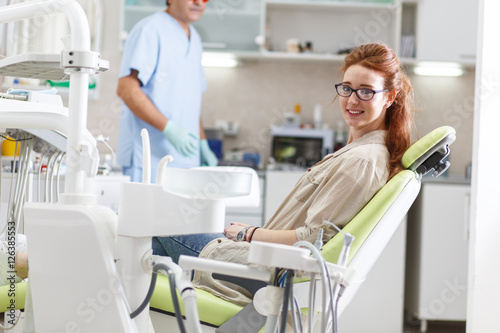 Young red hair female patient sitting on dental chair and preparing for treatment.