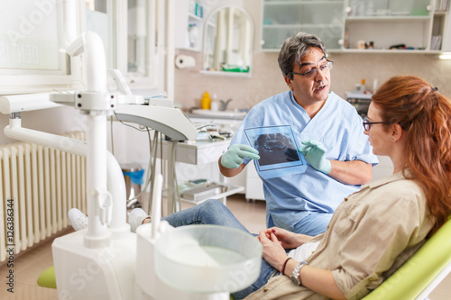 A professional dentist  equipped with a bright smile  converses with his red-haired female patient  carefully explaining the upcoming treatment  and ensuring her comfort throughout the process.